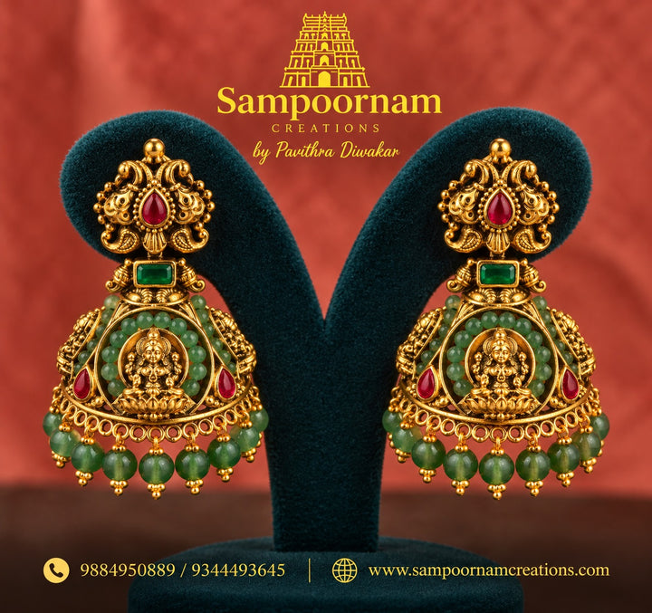 Temple Jewellery inspired Lakshmi Jhumka adorned with vibrant Green beeds and Rich Red Stone accents . Finished with cascading Green Bead hangings for a beautiful , traditional Festive Look .