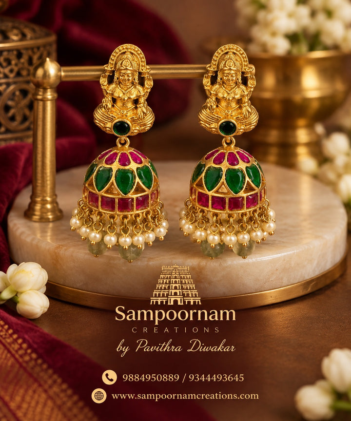 A Stunning Lakshmi motif Jhumka Adorned with Rich Green and Pink stones , delicate Pearl accents and Cascading Green bead Hangings .