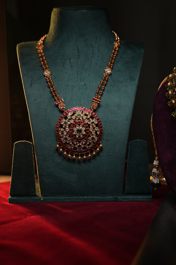 A Heritage Rakudi pendant with gold ball drops adorned with Jadau stones in white, green and red paired with a stone studded rettavari chain