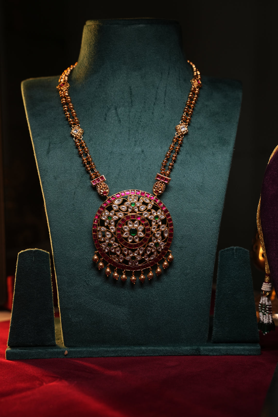 A Heritage Rakudi pendant with gold ball drops adorned with Jadau stones in white, green and red paired with a stone studded rettavari chain