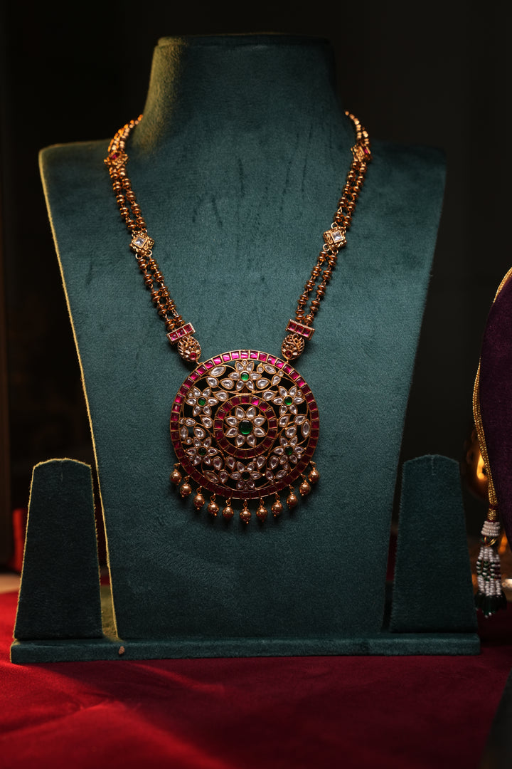 A Heritage Rakudi pendant with gold ball drops adorned with Jadau stones in white, green and red paired with a stone studded rettavari chain