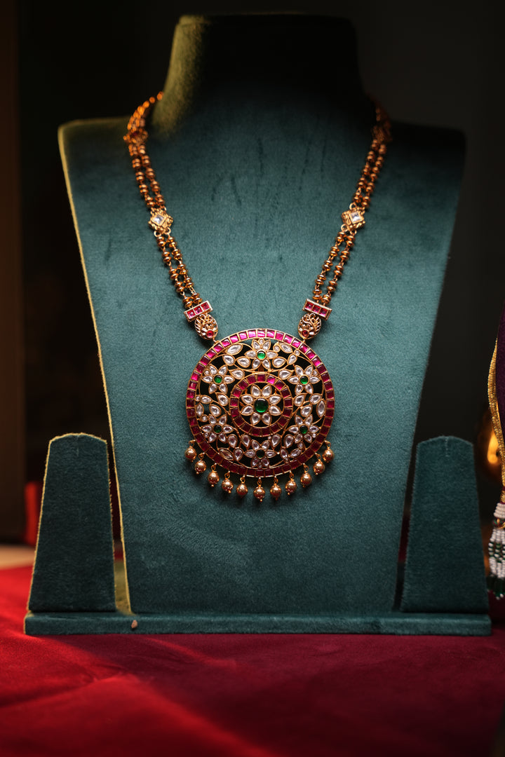A Heritage Rakudi pendant with gold ball drops adorned with Jadau stones in white, green and red paired with a stone studded rettavari chain