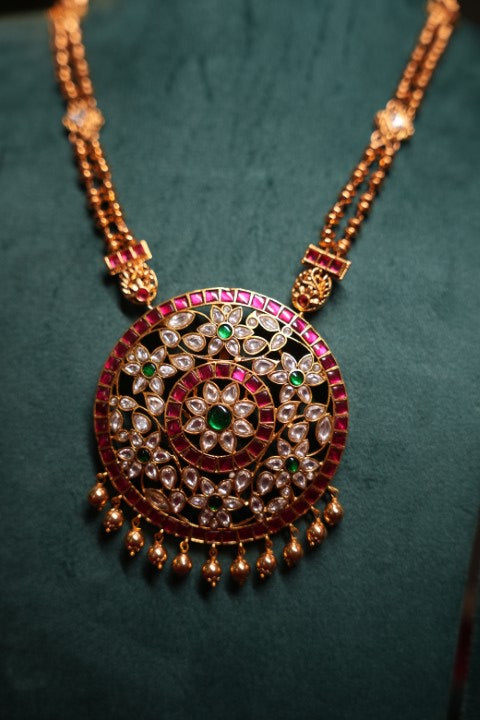 A Heritage Rakudi pendant with gold ball drops adorned with Jadau stones in white, green and red paired with a stone studded rettavari chain
