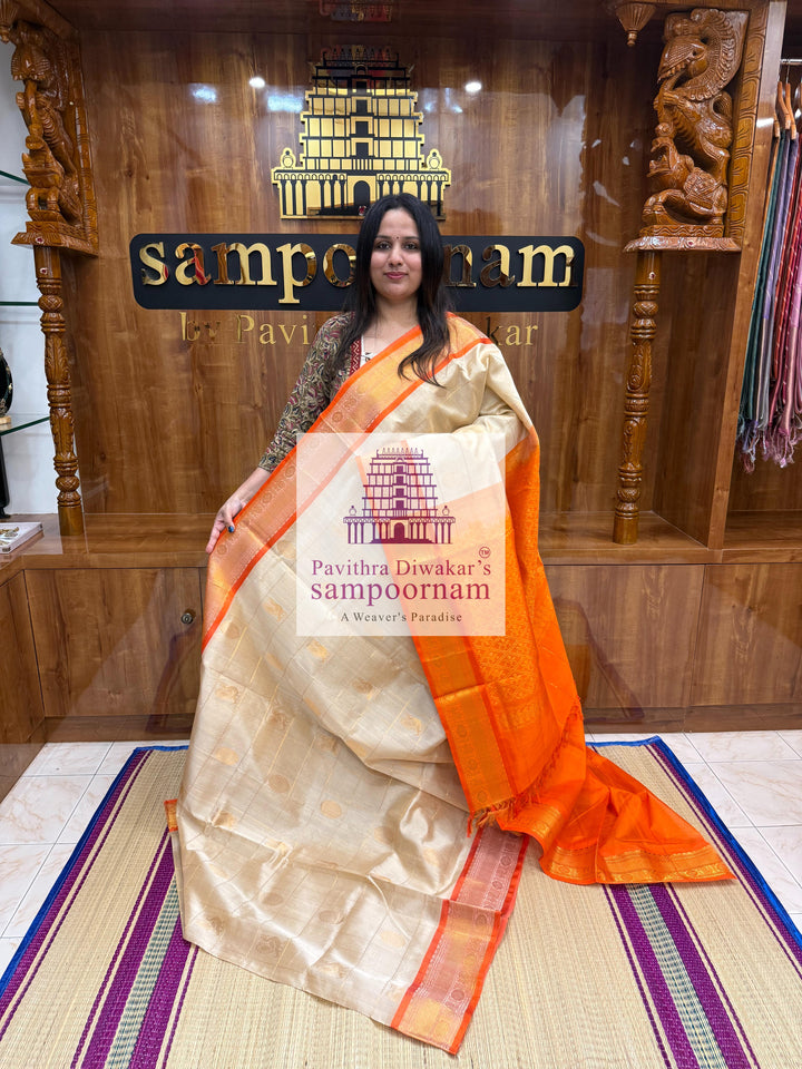 Offwhite with Orange , rich Zari checks in the body , Mayil and Chakram rich butta in the body , traditional borders and rich Pallu Silk Cotton Saree
