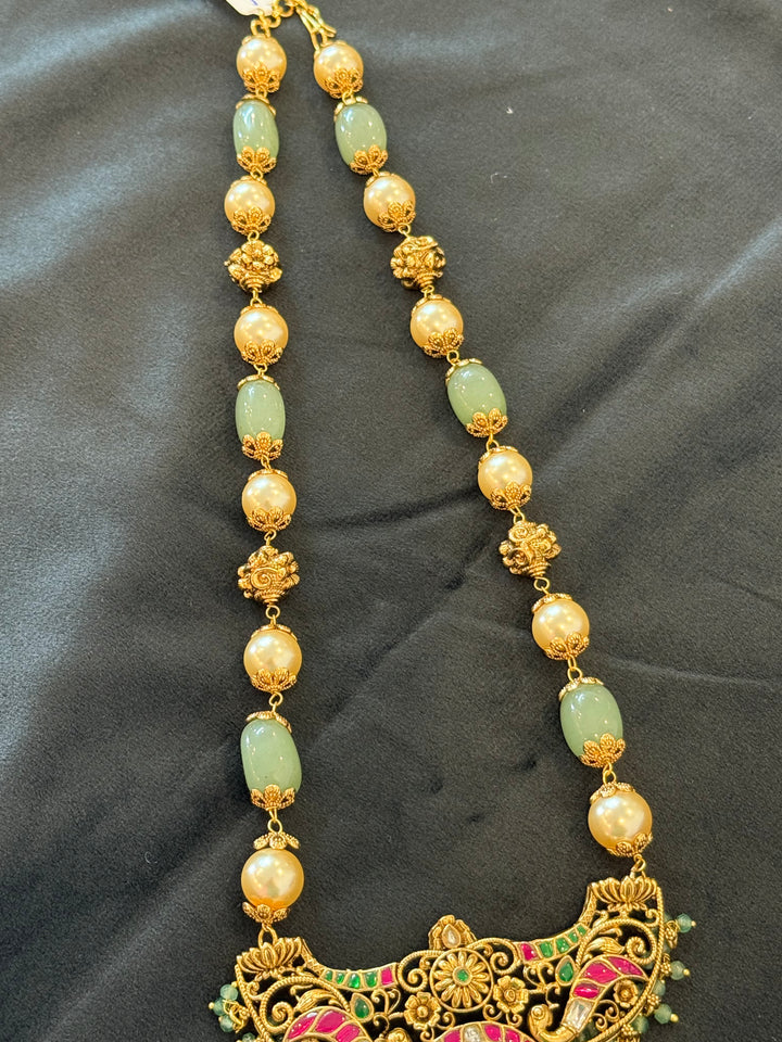 A regal pearl, gold, and emerald beaded necklace, completed with a magnificent three-layered Jadau pendant depicting Goddess Saraswati and Lord Ganesha. A classic pendant that elevates any traditional look.( With Jhumka )