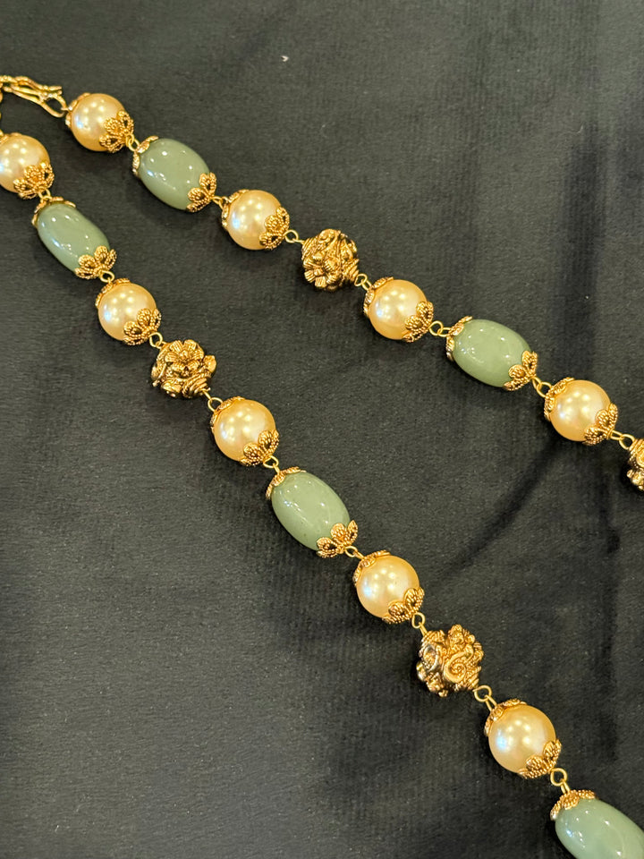 A regal pearl, gold, and emerald beaded necklace, completed with a magnificent three-layered Jadau pendant depicting Goddess Saraswati and Lord Ganesha. A classic pendant that elevates any traditional look.( With Jhumka )