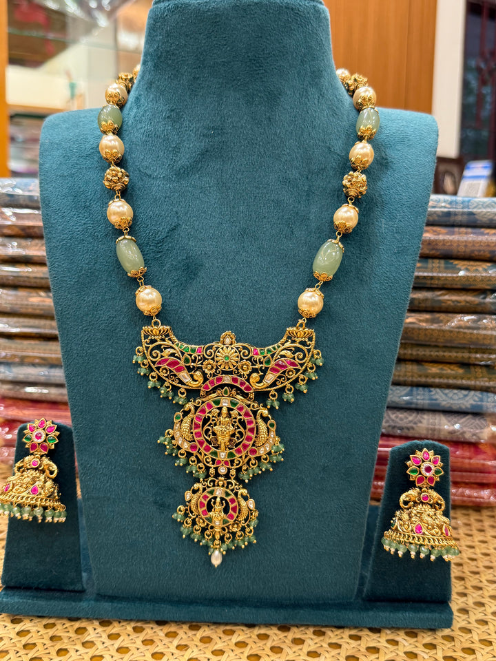 A regal pearl, gold, and emerald beaded necklace, completed with a magnificent three-layered Jadau pendant depicting Goddess Saraswati and Lord Ganesha. A classic pendant that elevates any traditional look.( With Jhumka )