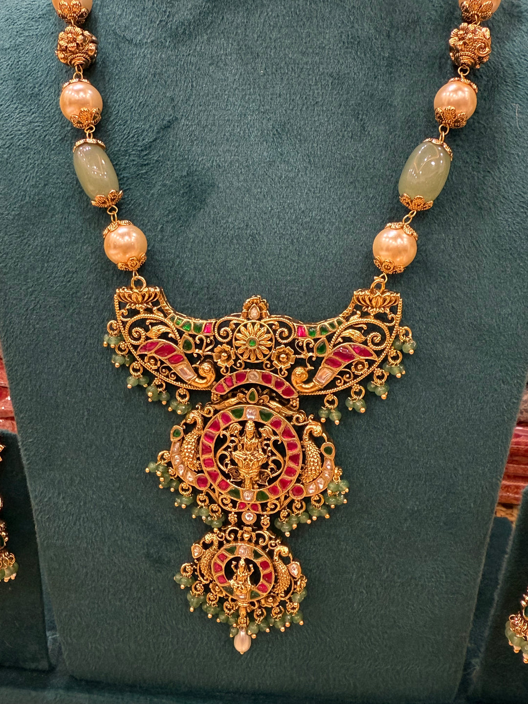 A regal pearl, gold, and emerald beaded necklace, completed with a magnificent three-layered Jadau pendant depicting Goddess Saraswati and Lord Ganesha. A classic pendant that elevates any traditional look.( With Jhumka )