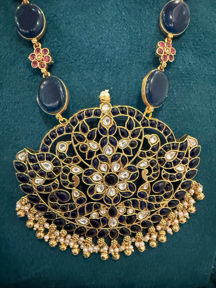 Our vintage blue pendant set, with rich blue & white kemp stones. The chain features blue stones and floral designs embellished with red and white stones. Paired with beautifully designed hanging earrings adorned with pearls and gold beads.