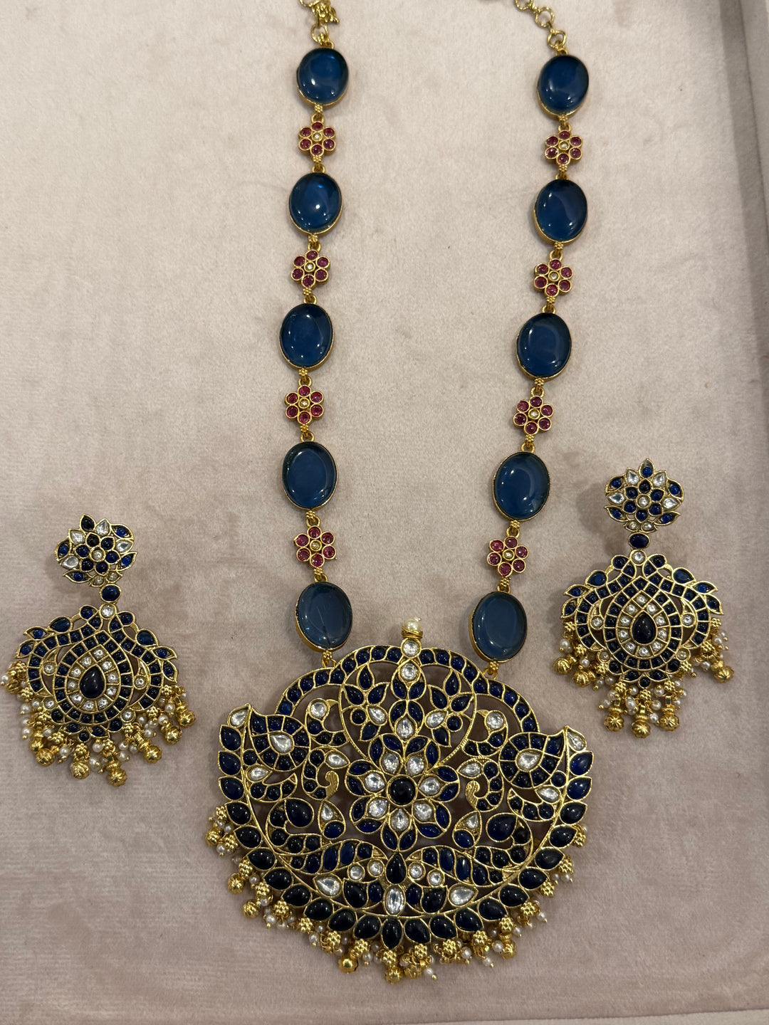 Our vintage blue pendant set, with rich blue & white kemp stones. The chain features blue stones and floral designs embellished with red and white stones. Paired with beautifully designed hanging earrings adorned with pearls and gold beads.