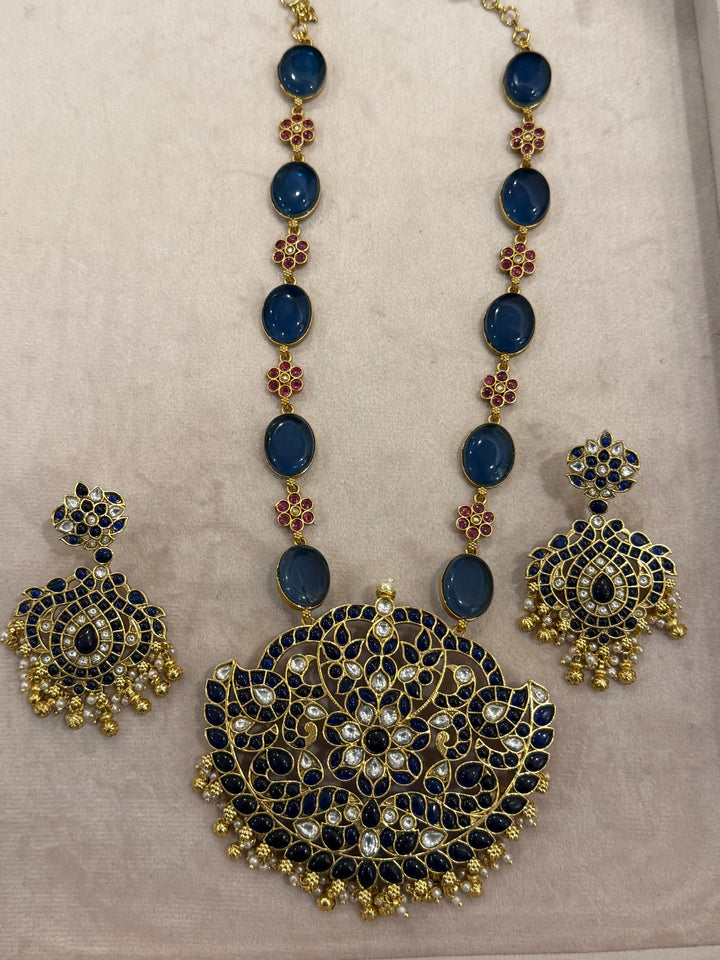 Our vintage blue pendant set, with rich blue & white kemp stones. The chain features blue stones and floral designs embellished with red and white stones. Paired with beautifully designed hanging earrings adorned with pearls and gold beads.