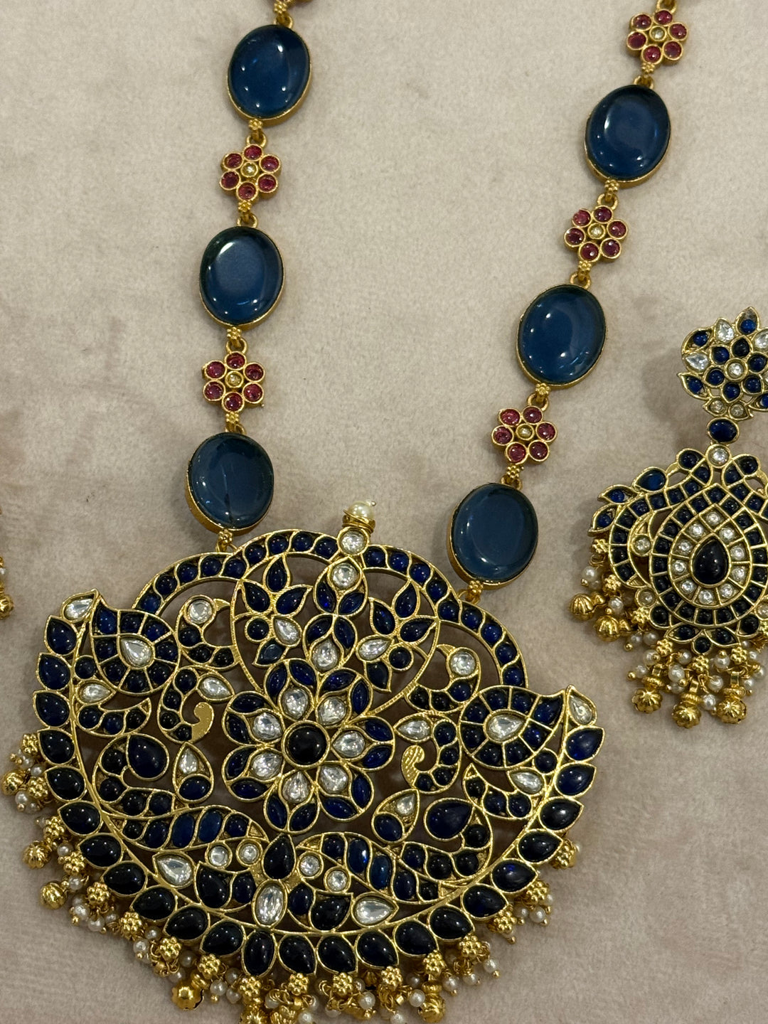 Our vintage blue pendant set, with rich blue & white kemp stones. The chain features blue stones and floral designs embellished with red and white stones. Paired with beautifully designed hanging earrings adorned with pearls and gold beads.