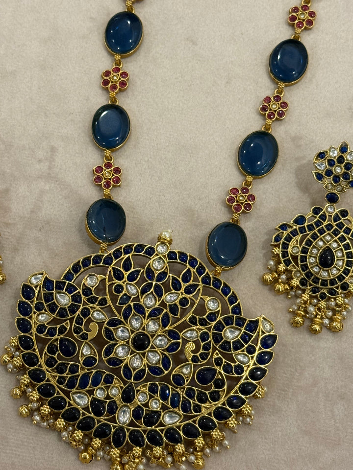 Our vintage blue pendant set, with rich blue & white kemp stones. The chain features blue stones and floral designs embellished with red and white stones. Paired with beautifully designed hanging earrings adorned with pearls and gold beads.