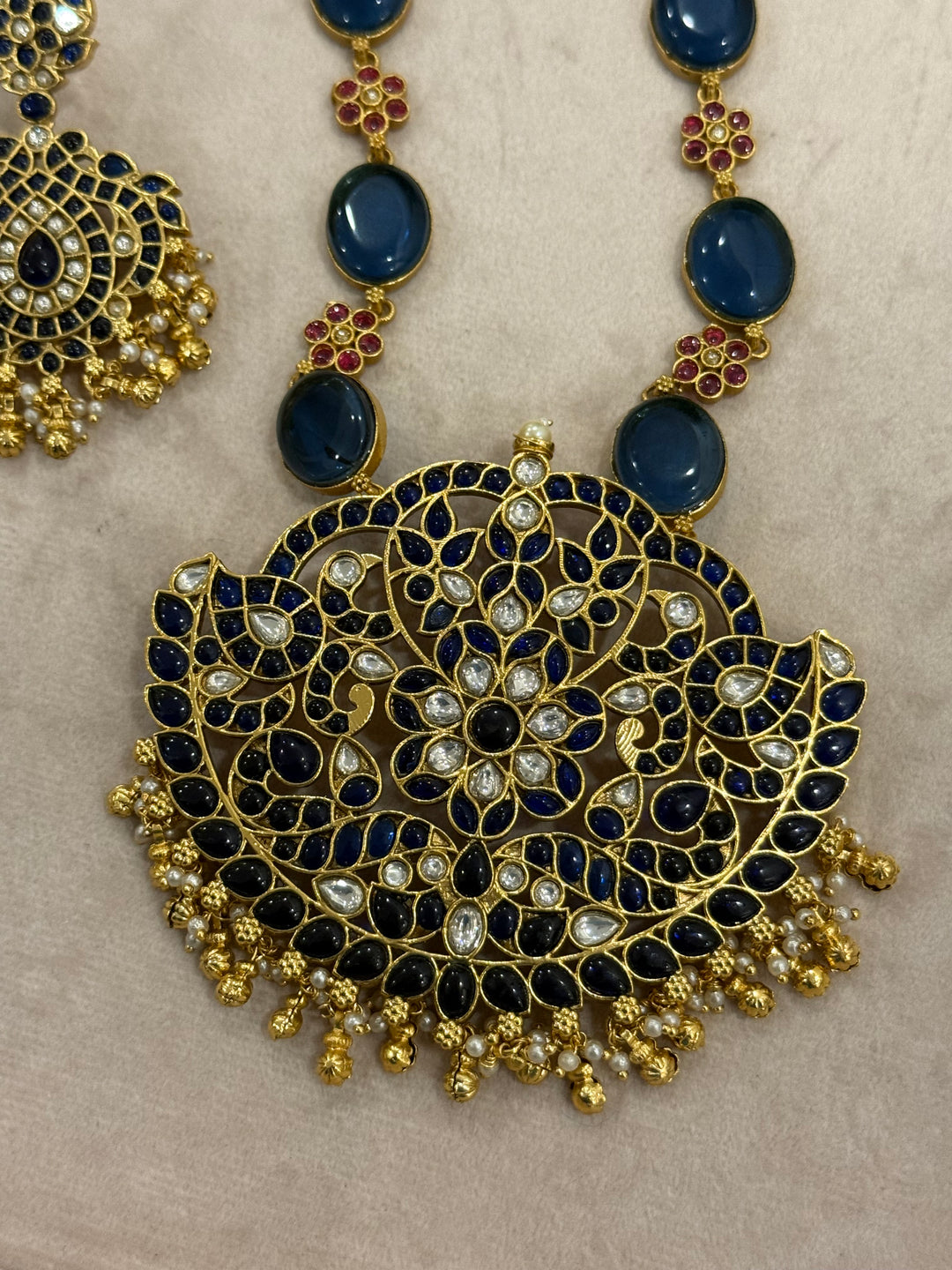 Our vintage blue pendant set, with rich blue & white kemp stones. The chain features blue stones and floral designs embellished with red and white stones. Paired with beautifully designed hanging earrings adorned with pearls and gold beads.