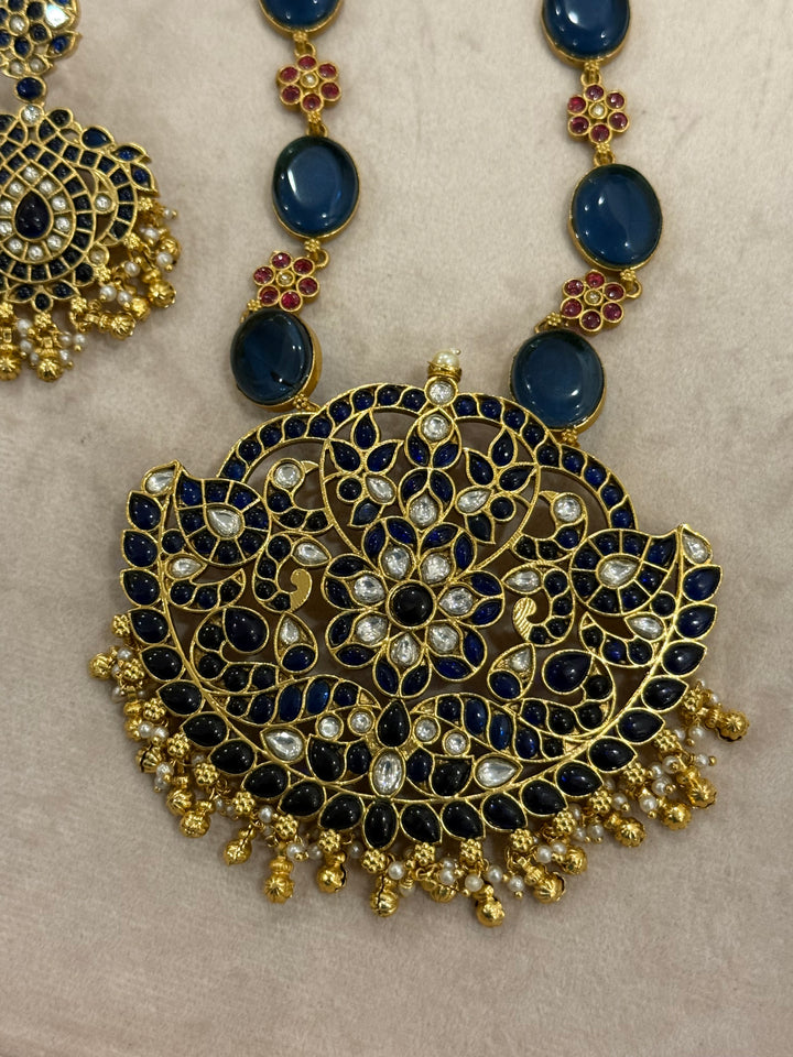 Our vintage blue pendant set, with rich blue & white kemp stones. The chain features blue stones and floral designs embellished with red and white stones. Paired with beautifully designed hanging earrings adorned with pearls and gold beads.