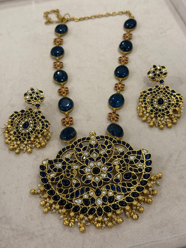 Our vintage blue pendant set, with rich blue & white kemp stones. The chain features blue stones and floral designs embellished with red and white stones. Paired with beautifully designed hanging earrings adorned with pearls and gold beads.