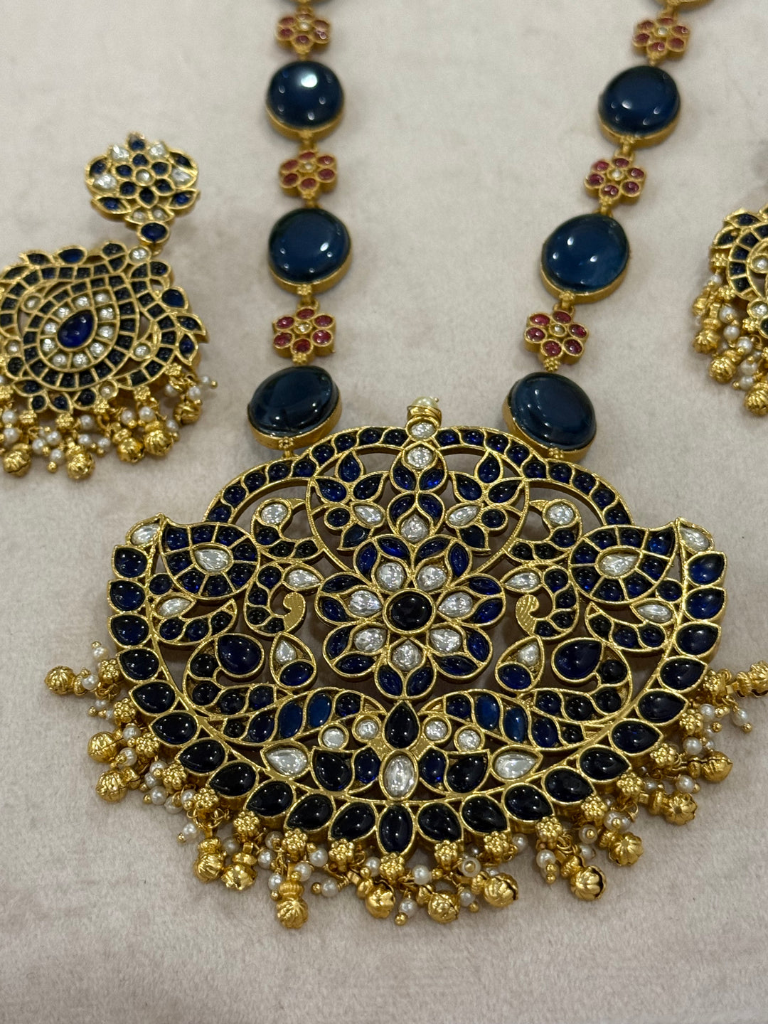 Our vintage blue pendant set, with rich blue & white kemp stones. The chain features blue stones and floral designs embellished with red and white stones. Paired with beautifully designed hanging earrings adorned with pearls and gold beads.