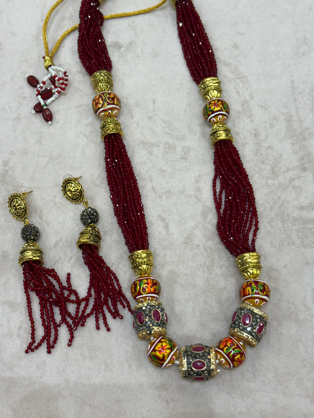 Dark Red multi crystal bead stranded neckpiece adorned with antique gold elements and intricate meenakari balls, paired with tassel shaped eardrops