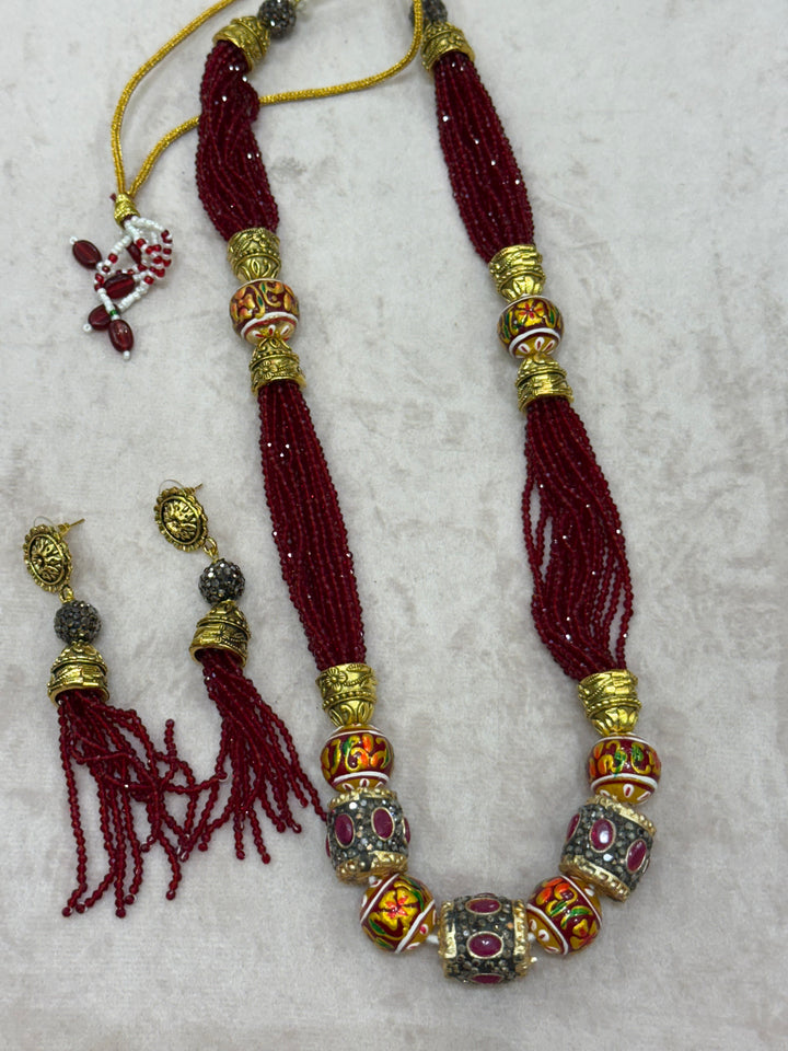 Dark Red multi crystal bead stranded neckpiece adorned with antique gold elements and intricate meenakari balls, paired with tassel shaped eardrops