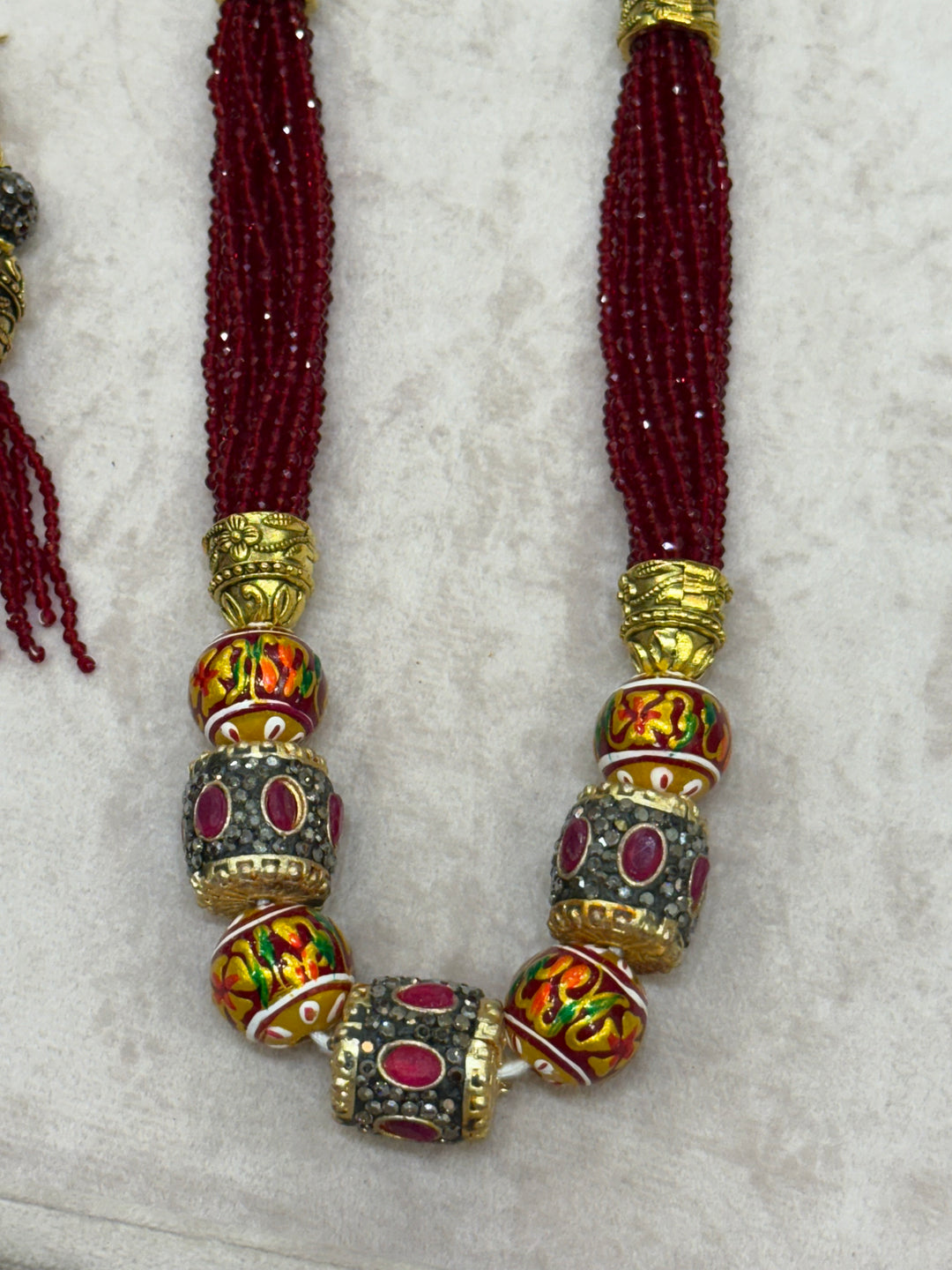 Dark Red multi crystal bead stranded neckpiece adorned with antique gold elements and intricate meenakari balls, paired with tassel shaped eardrops