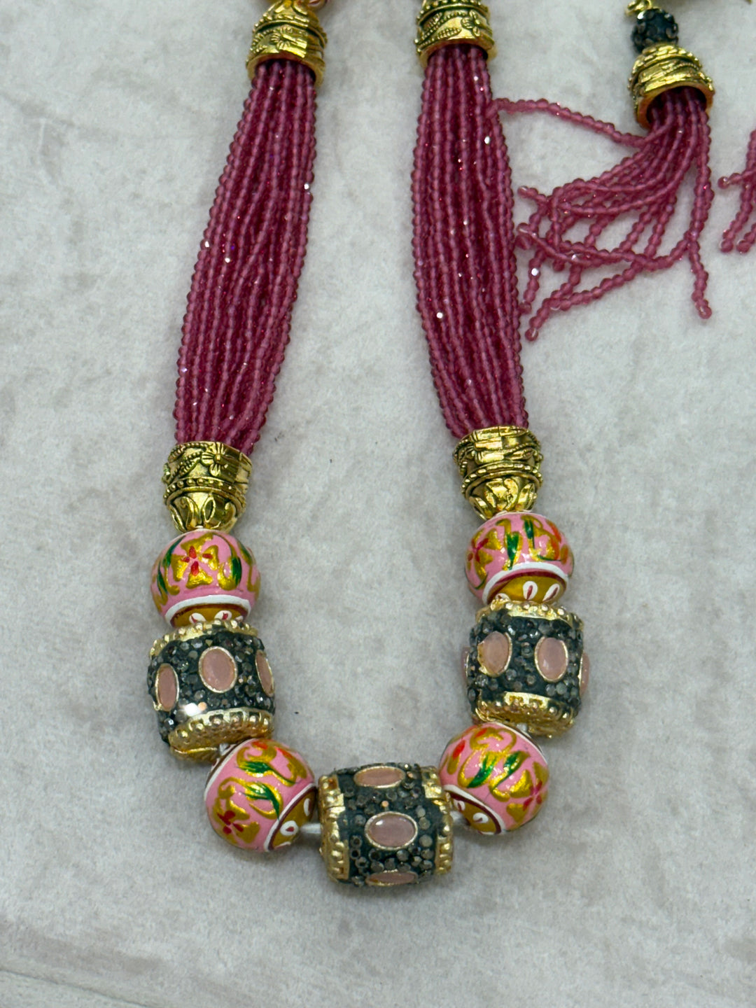 Pink multi crystal bead stranded neckpiece adorned with antique gold elements and intricate meenakari balls, paired with tassel shaped ear drops.