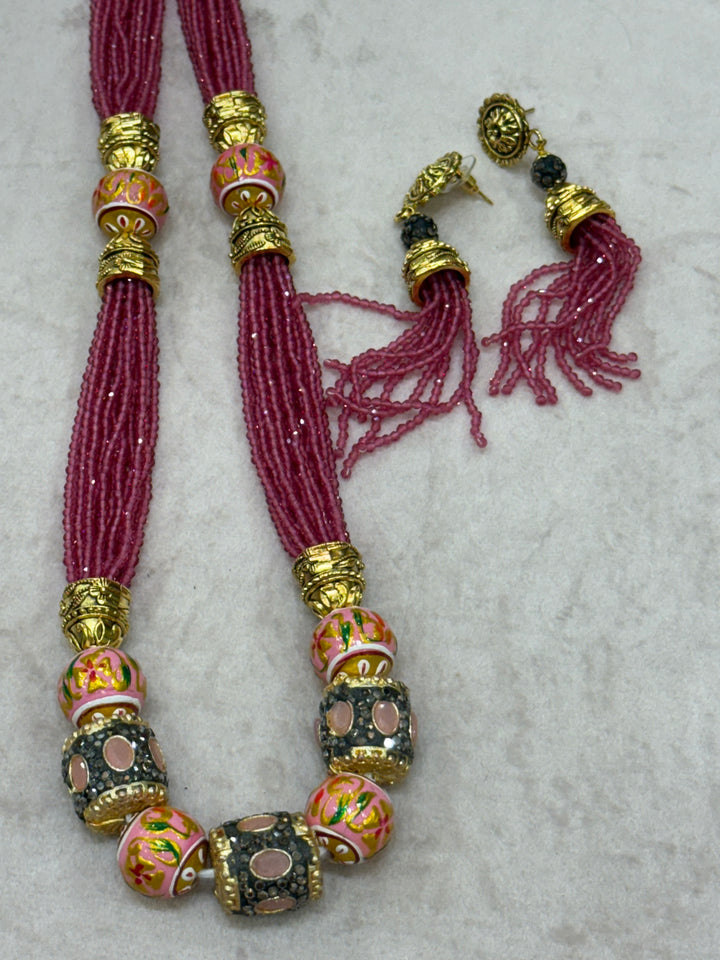 Pink multi crystal bead stranded neckpiece adorned with antique gold elements and intricate meenakari balls, paired with tassel shaped ear drops.