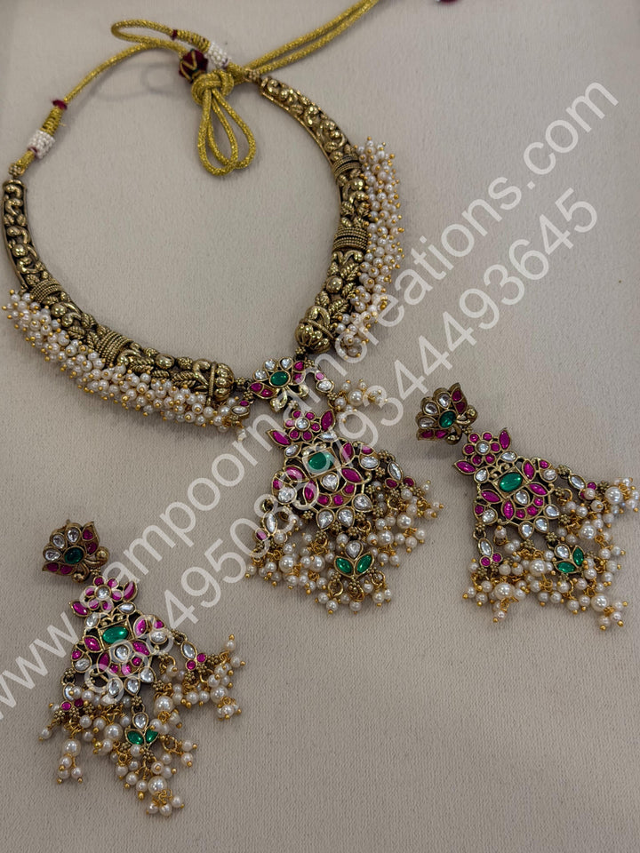 An exquisite antique finish jadau choker, intricately detailed with red, green and white stones, cascading pearls,with a statement pendant and floral jhumka inspired earings.