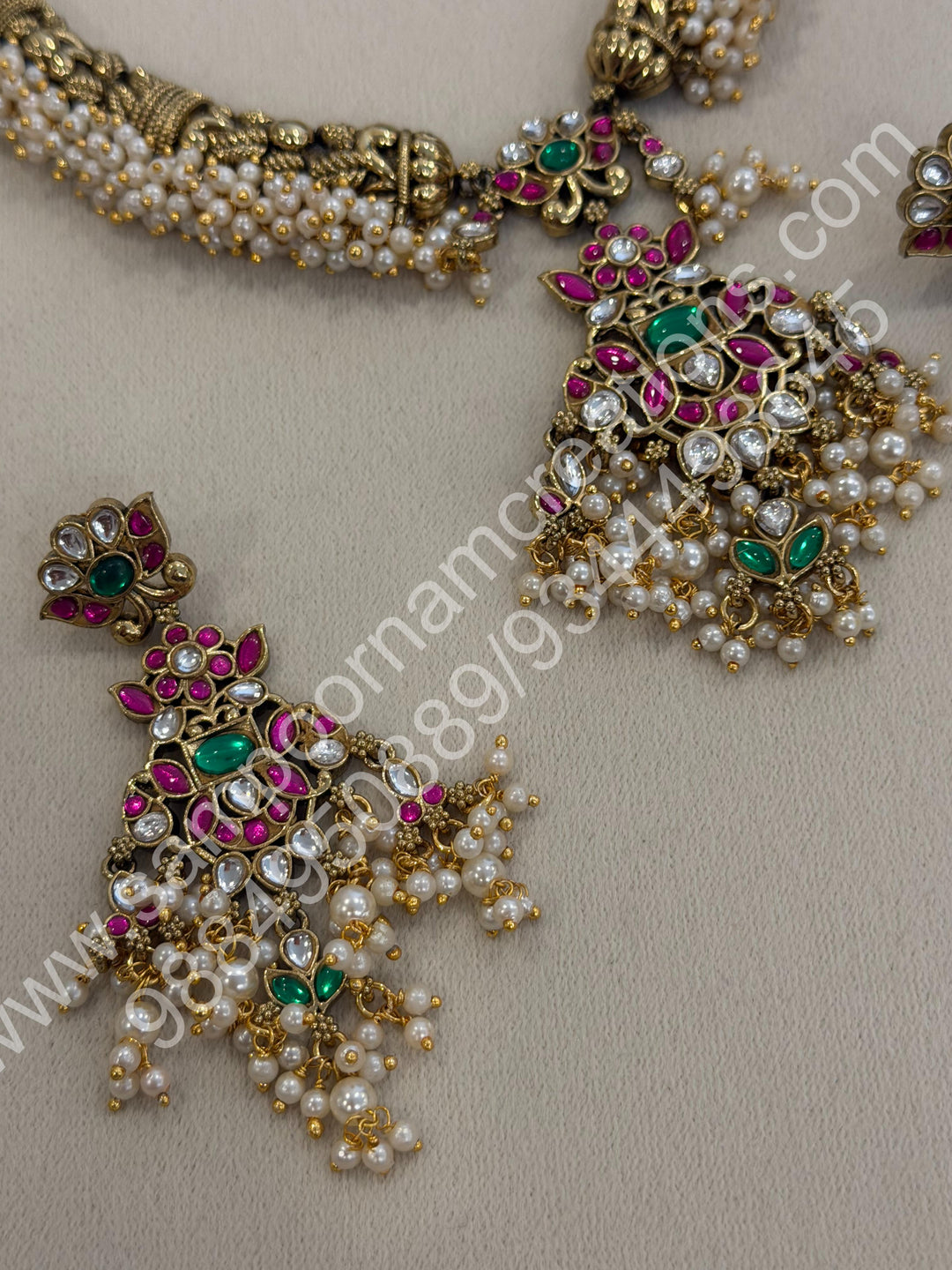 An exquisite antique finish jadau choker, intricately detailed with red, green and white stones, cascading pearls,with a statement pendant and floral jhumka inspired earings.