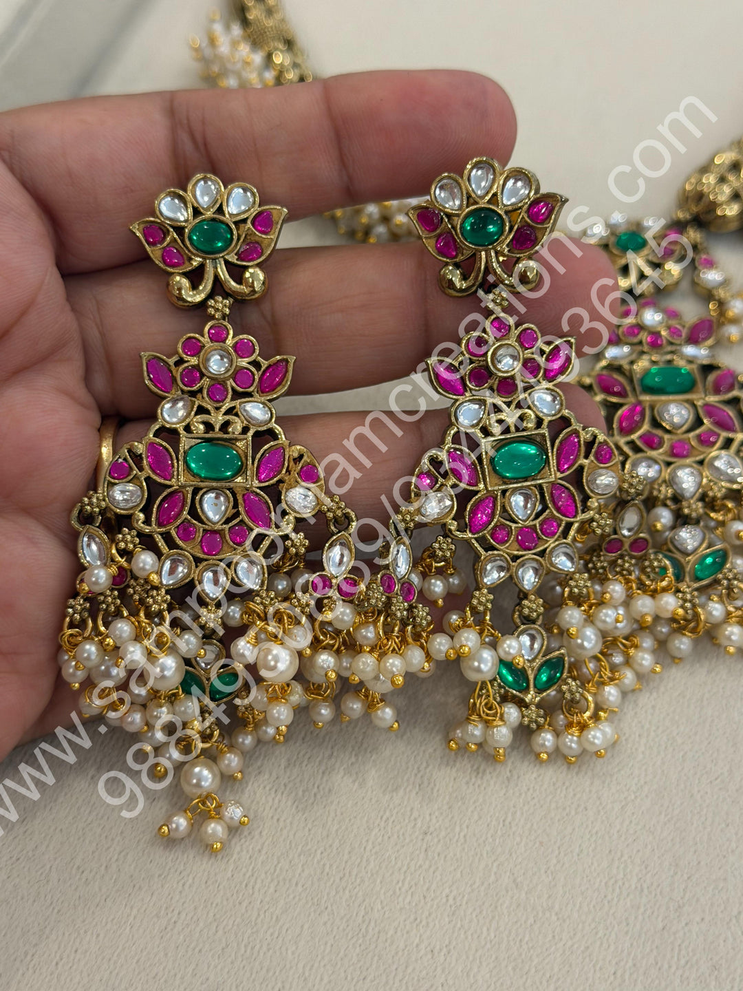 An exquisite antique finish jadau choker, intricately detailed with red, green and white stones, cascading pearls,with a statement pendant and floral jhumka inspired earings.