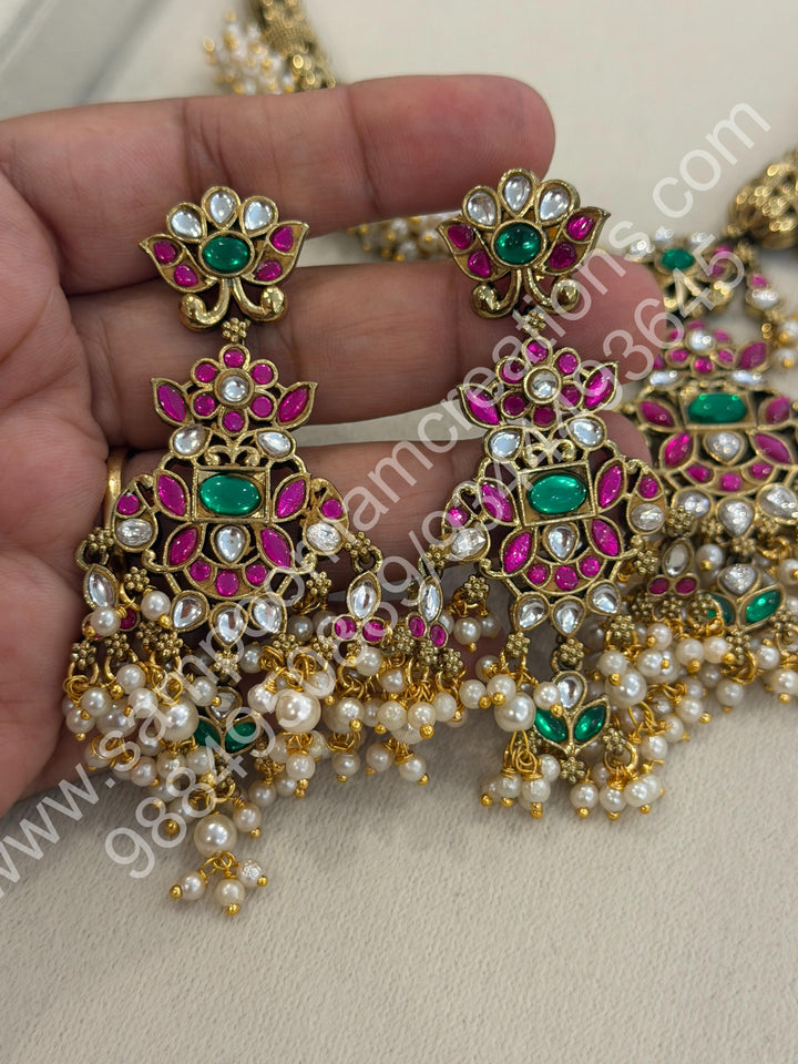 An exquisite antique finish jadau choker, intricately detailed with red, green and white stones, cascading pearls,with a statement pendant and floral jhumka inspired earings.