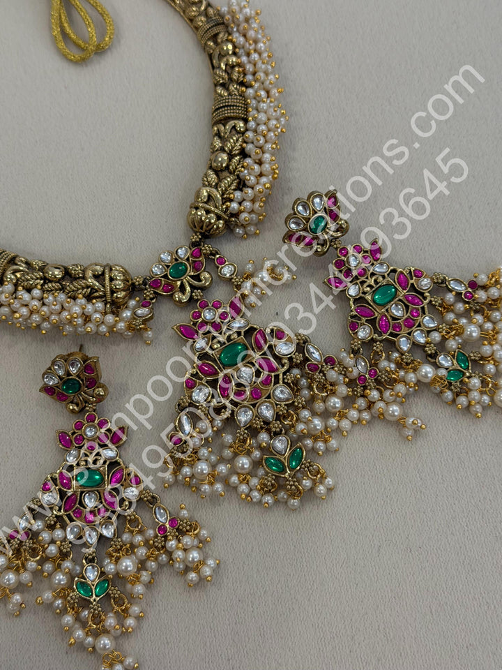 An exquisite antique finish jadau choker, intricately detailed with red, green and white stones, cascading pearls,with a statement pendant and floral jhumka inspired earings.