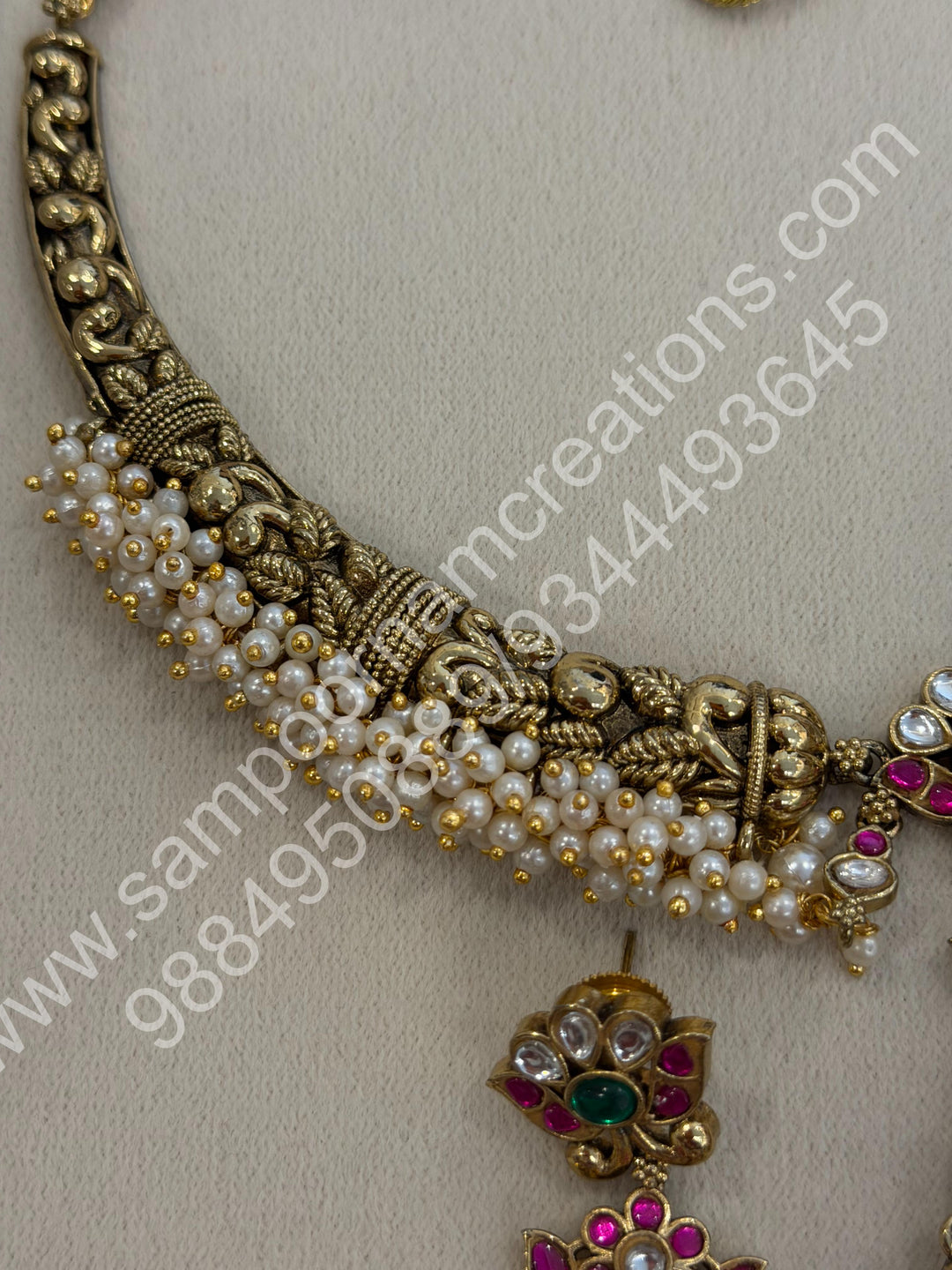 An exquisite antique finish jadau choker, intricately detailed with red, green and white stones, cascading pearls,with a statement pendant and floral jhumka inspired earings.