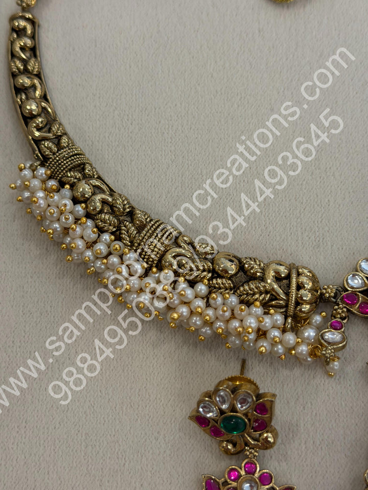 An exquisite antique finish jadau choker, intricately detailed with red, green and white stones, cascading pearls,with a statement pendant and floral jhumka inspired earings.