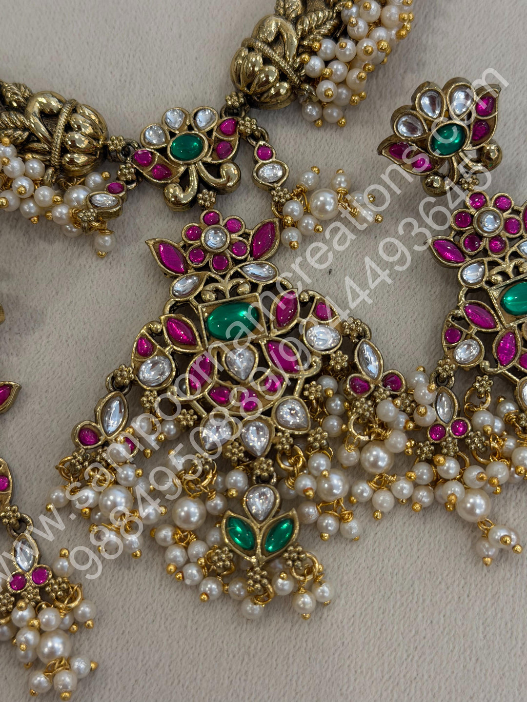 An exquisite antique finish jadau choker, intricately detailed with red, green and white stones, cascading pearls,with a statement pendant and floral jhumka inspired earings.