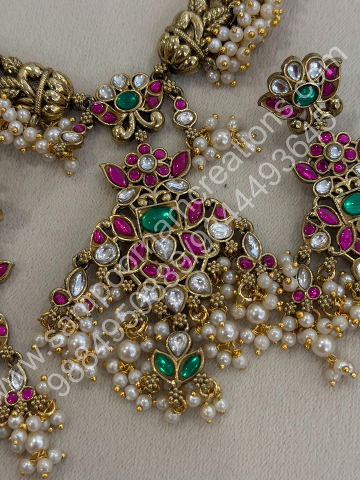 An exquisite antique finish jadau choker, intricately detailed with red, green and white stones, cascading pearls,with a statement pendant and floral jhumka inspired earings.