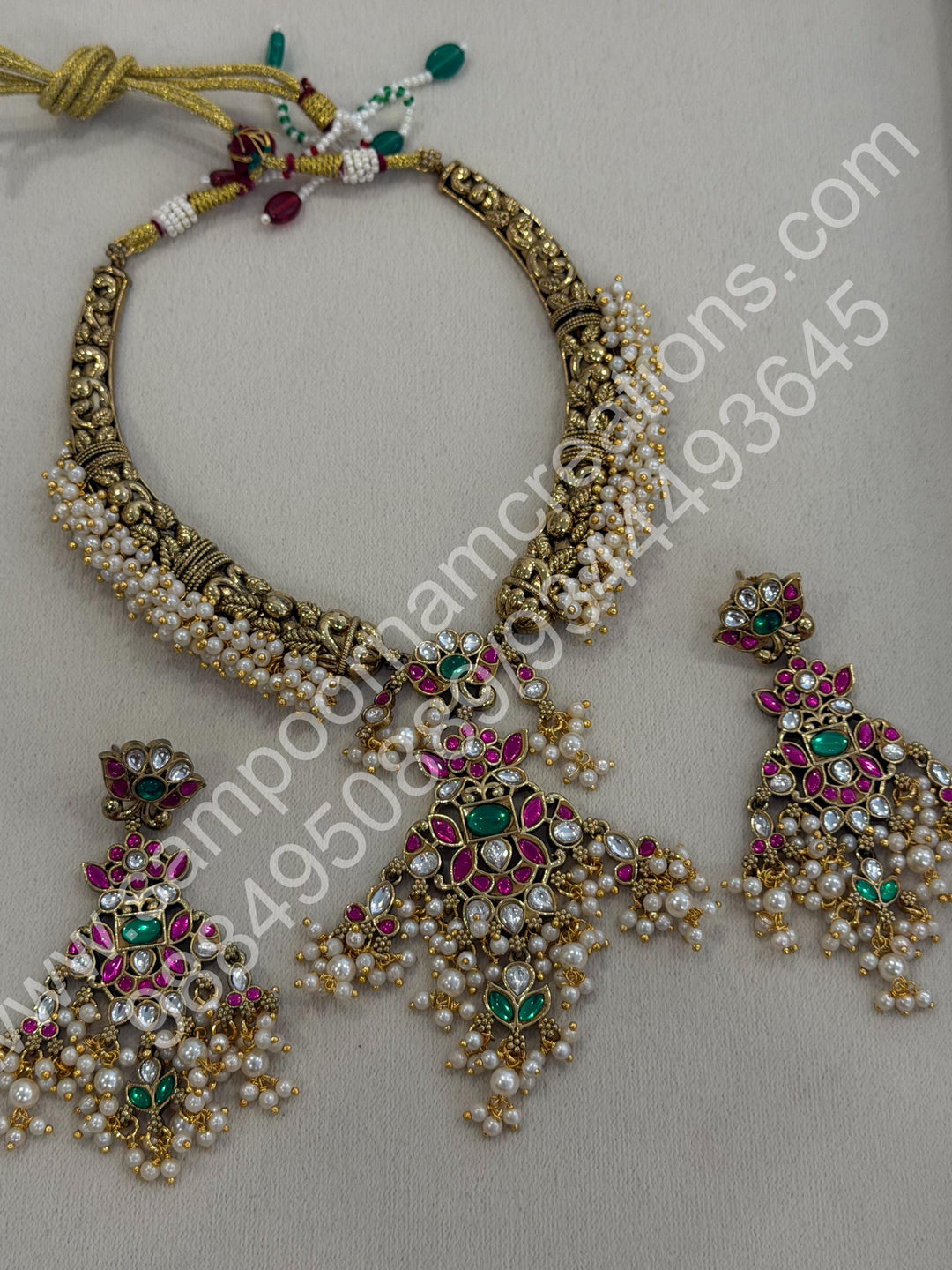 An exquisite antique finish jadau choker, intricately detailed with red, green and white stones, cascading pearls,with a statement pendant and floral jhumka inspired earings.