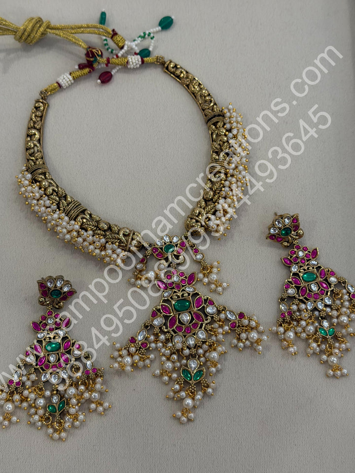 An exquisite antique finish jadau choker, intricately detailed with red, green and white stones, cascading pearls,with a statement pendant and floral jhumka inspired earings.