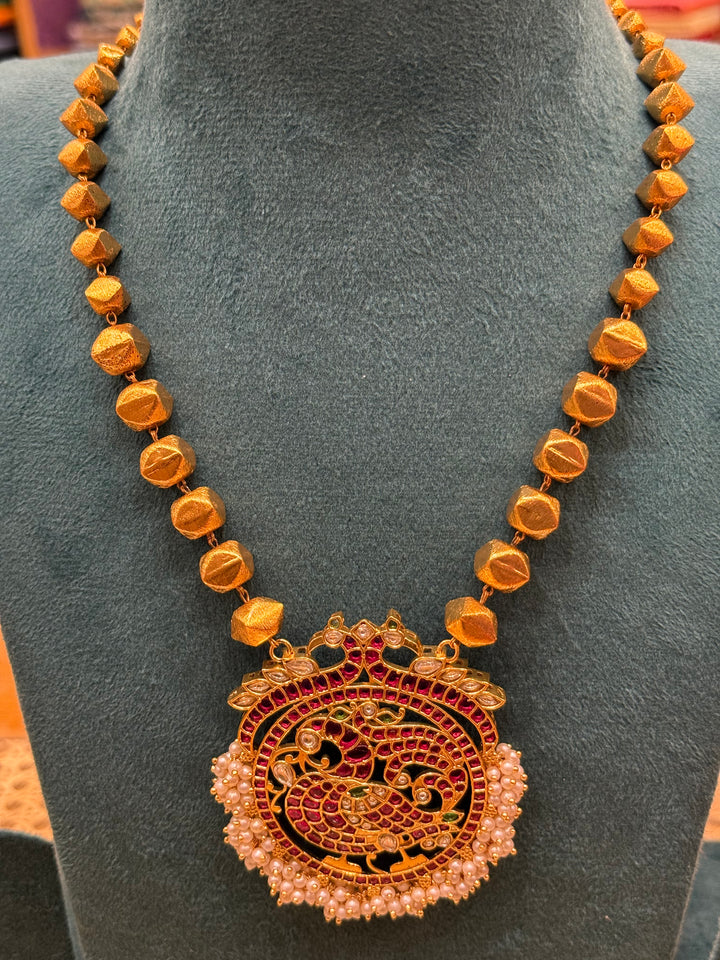 A Piece where tradition gets a bold upgrade , 3D gold beads flows is graduating sizes, Annam pendant detailed with Red Green and White Kemp Stones and delicate adduku white pearls .